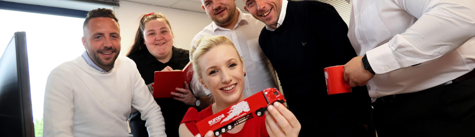 The Europa Road Cardiff team are all facing the camera. Branch manager Chelsea is holding a red, branded Europa truck.