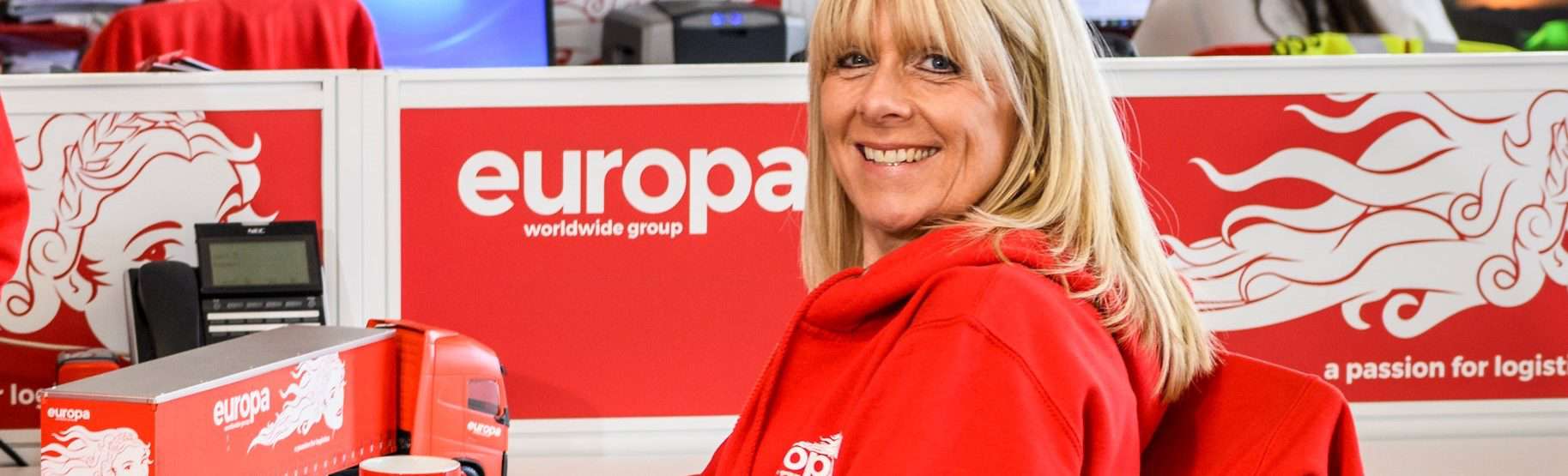 Angie Recce sits in Europa branded red hoodie, smiling at the camera