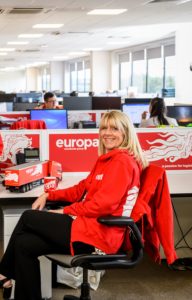 Angie Recce sits in Europa branded red hoodie, smiling at the camera