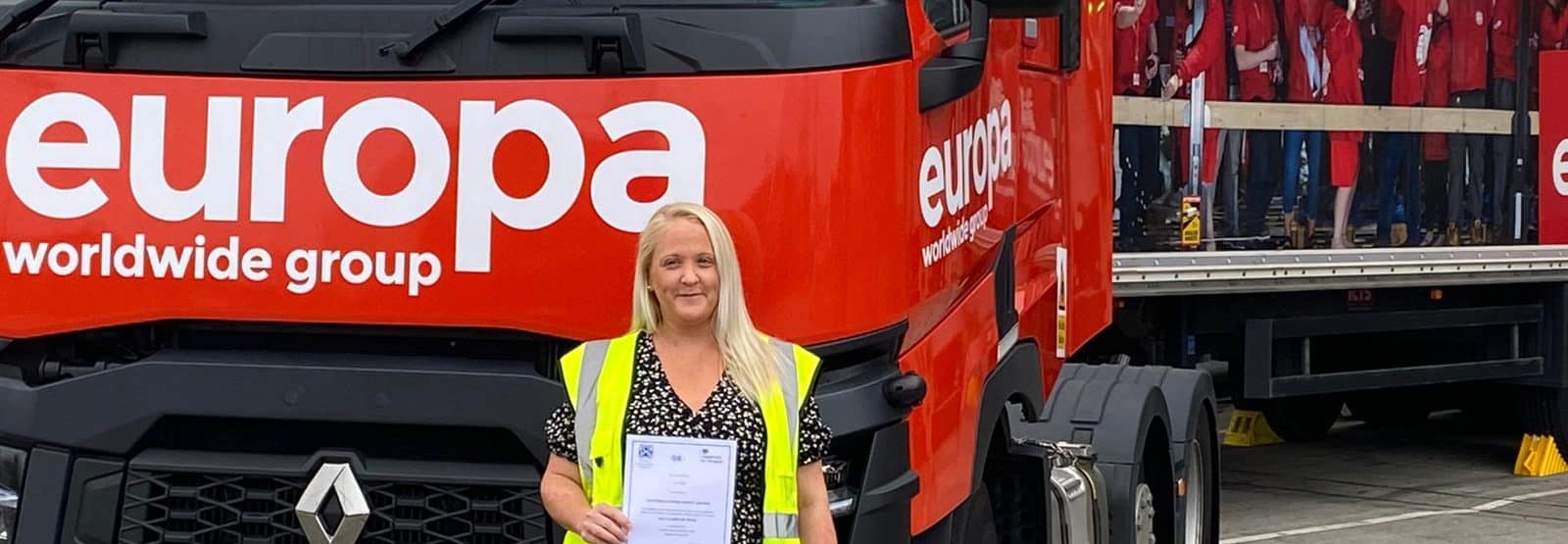 Sarah Elliott stands in HiVis, in front of a Europa truck, holding her DGSA.