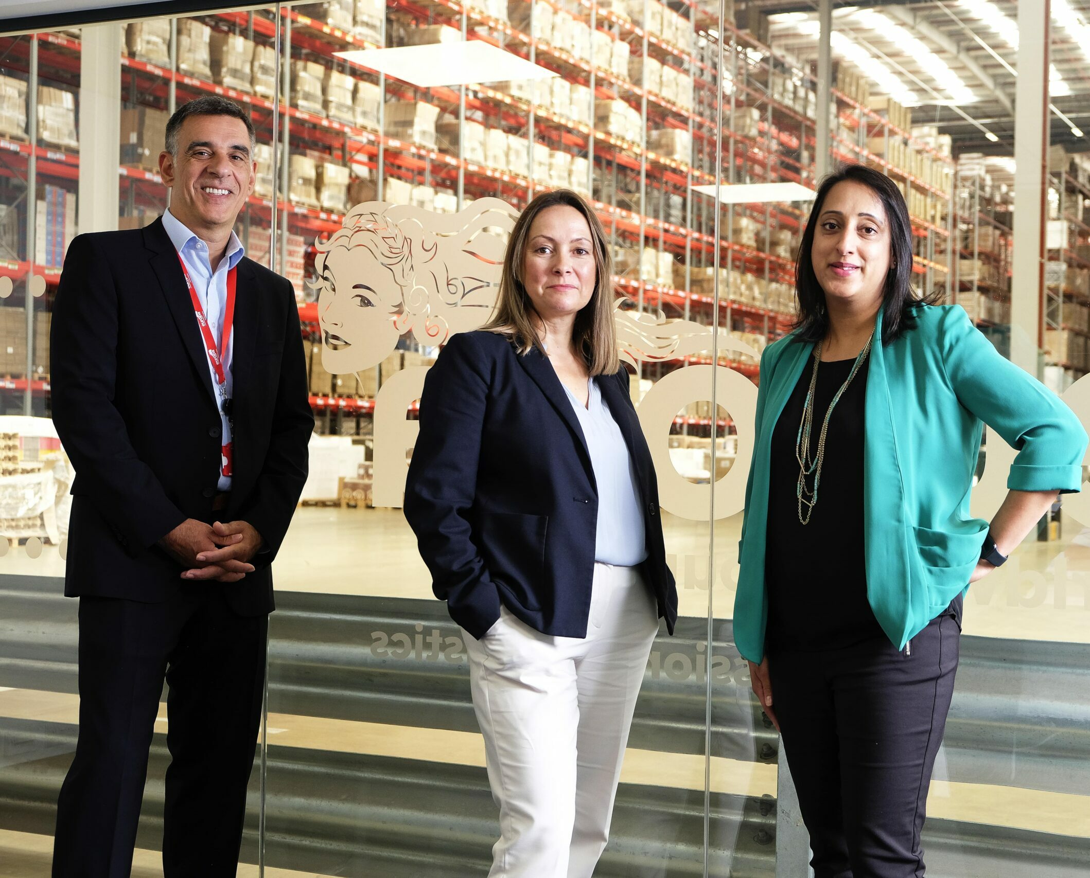 John, Sally and Sonal stand in front of a glass wall inside a Europa Warehouse.
